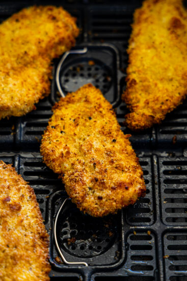 Air fried chicken cutlets in air fryer basket.