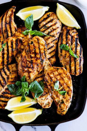 Grilled chicken breasts in grill pan with lemon and basil.