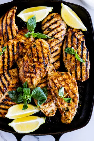 Grilled chicken breasts in grill pan with lemon and basil.
