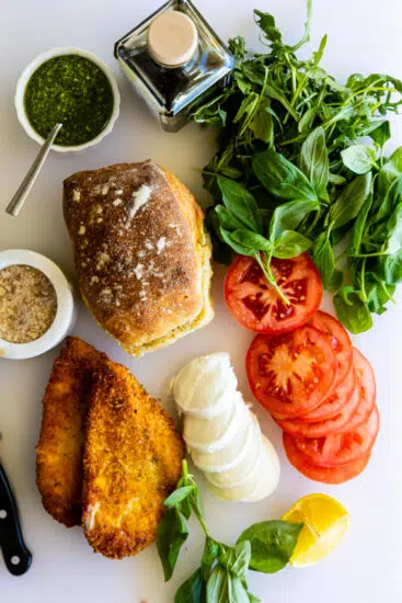 Ingredients for a chicken caprese sandwich on a white chopping board.