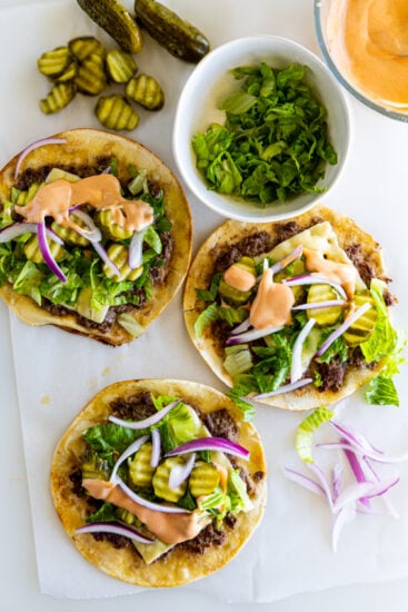 Smashed burger tacos with burger sauce, pickles, onions and lettuce.