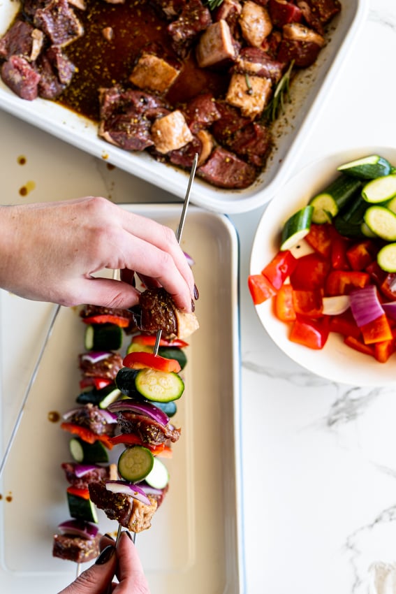 Threading marinated steak with peppers and zucchini onto skewers.
