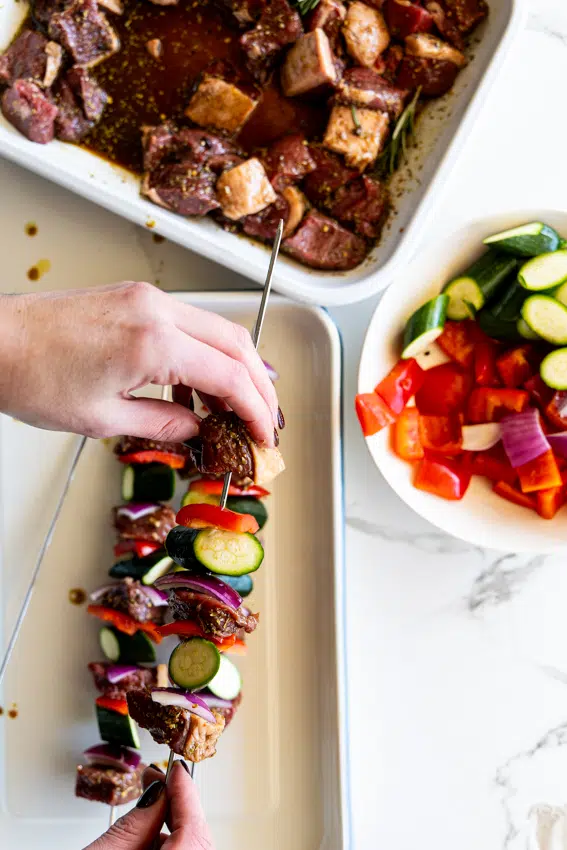 Threading marinated steak with peppers and zucchini onto skewers.