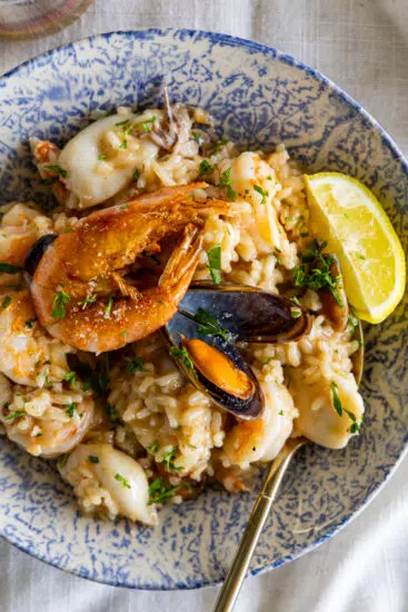 Seafood risotto in serving bowl with lemon wedge.