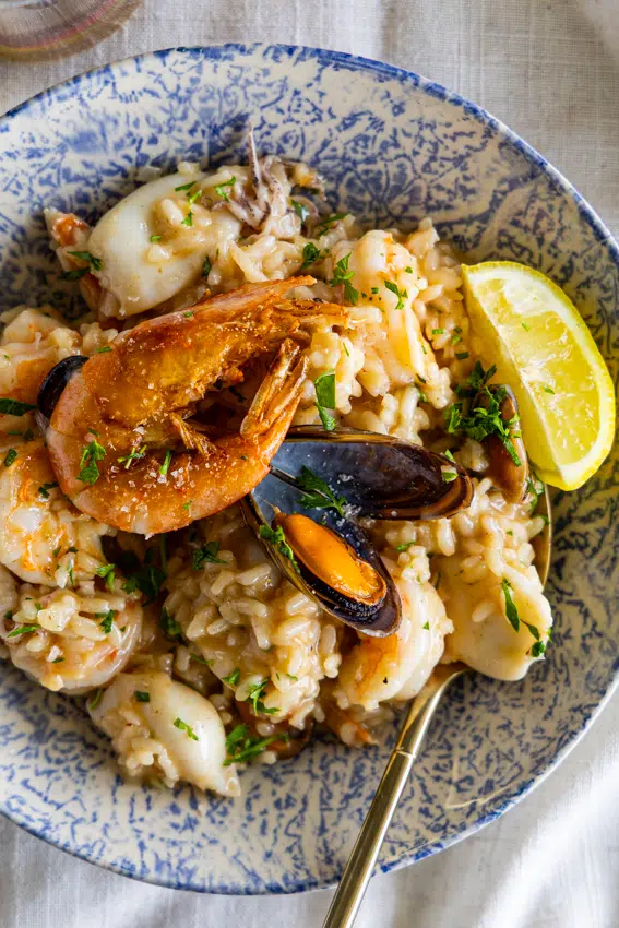 Seafood risotto in serving bowl with lemon wedge.
