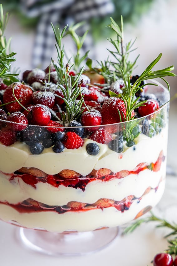 Christmas trifle with fresh berries, cream, and ladyfingers garnished with rosemary.