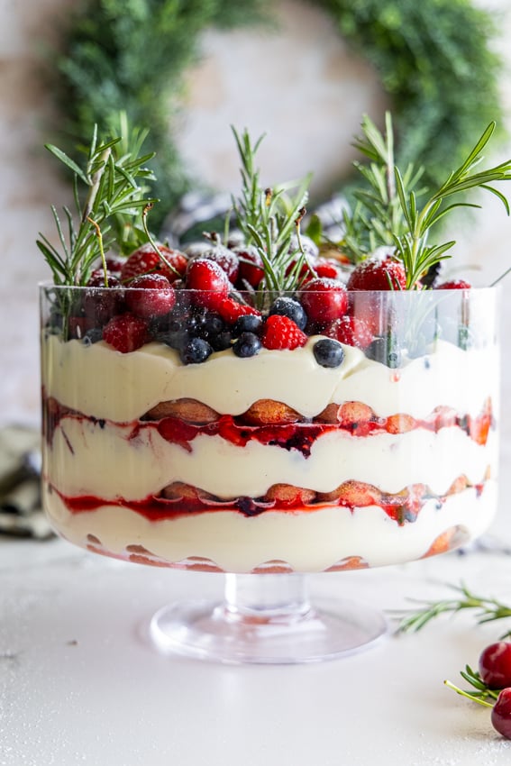 Festive berry tiramisu trifle in clear glass bowl showing layers.