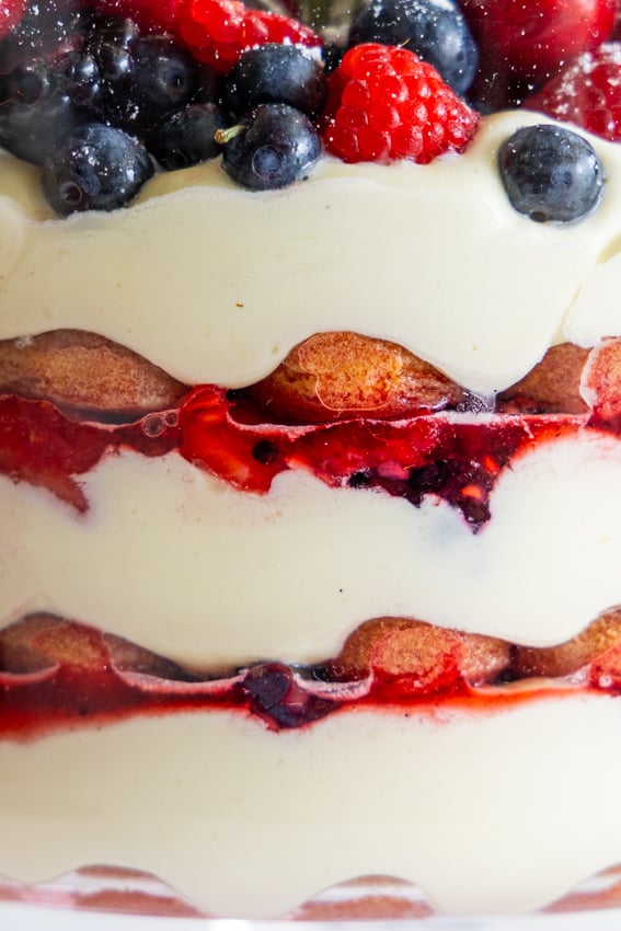 Festive berry tiramisu trifle in clear glass bowl showing layers.