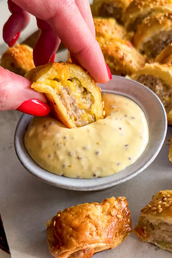 Close up of hand holding spicy sausage roll showing pork and cheese filling