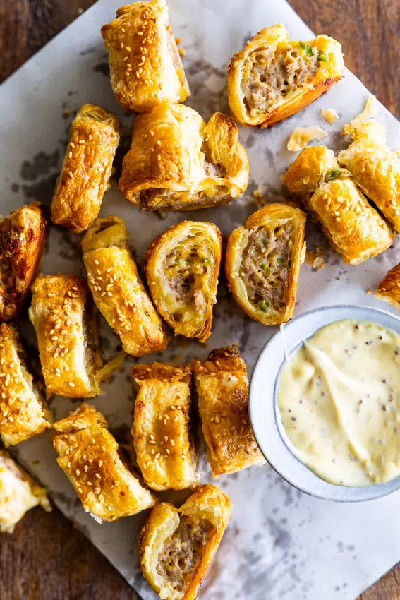 Golden brown jalapeño cheddar sausage rolls with sesame seeds on serving platter with dipping sauce.