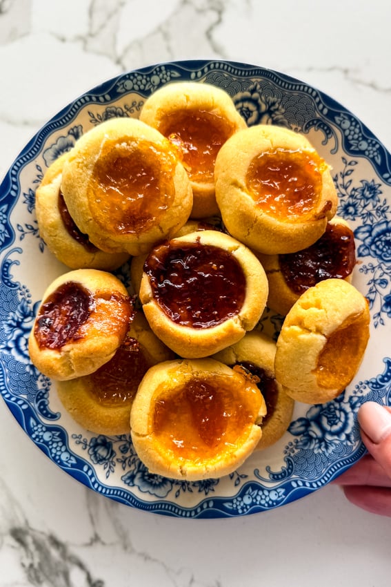 Shortbread thumbprint cookies with raspberry and apricot jam on blue and white plate.