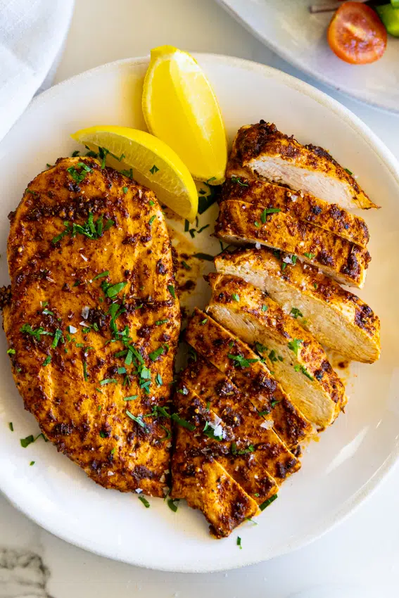 Juicy air fryer chicken breast on a white plate with lemon wedges.