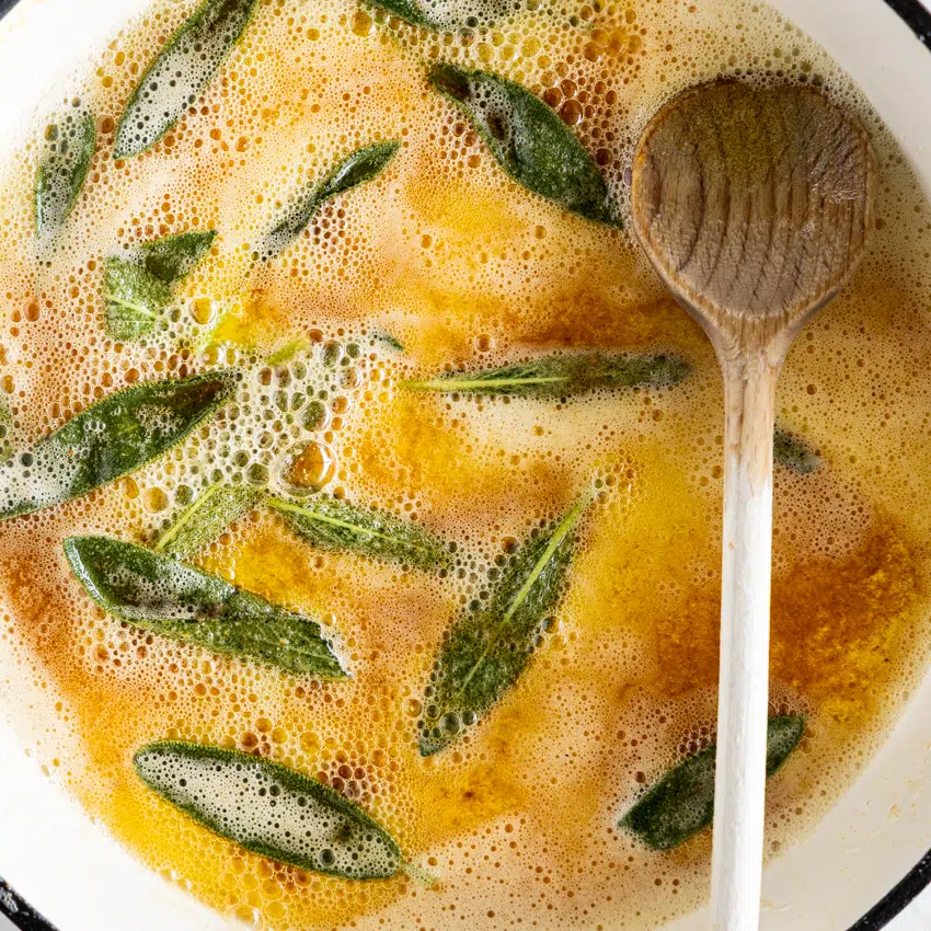 Brown butter sage sauce in a frying pan with wooden spoon.