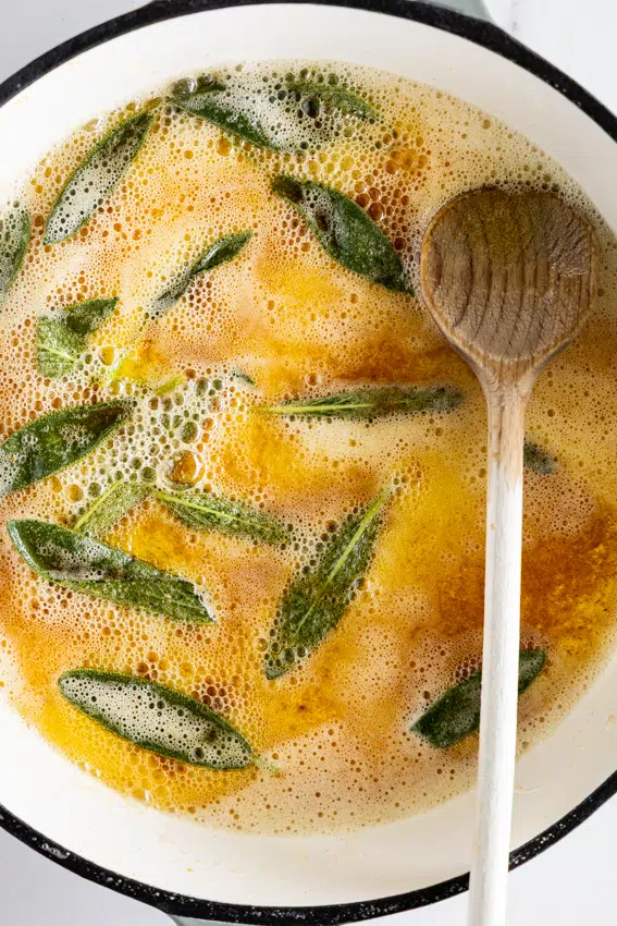 Brown butter sage sauce in frying pan with wooden spoon.