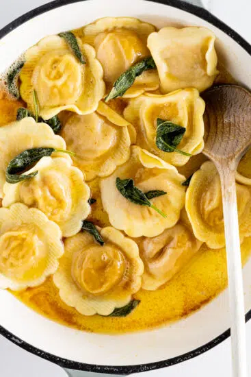 Brown butter sage sauce with ravioli in pan.