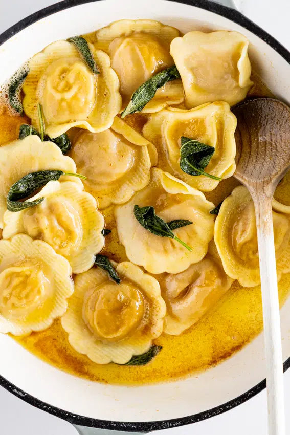 Brown butter sage sauce with ravioli in pan.