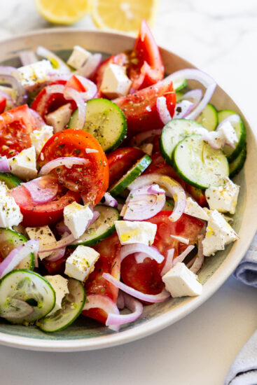 Cucumber tomato and feta salad on a white marble table with lemons.