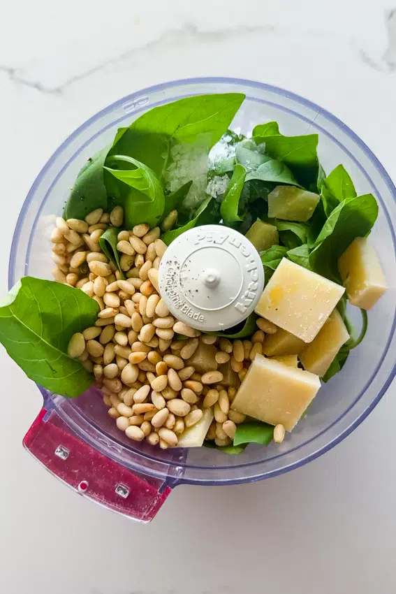 Fresh basil, toasted pine nuts and parmesan cheese in the bowl of a food processor.