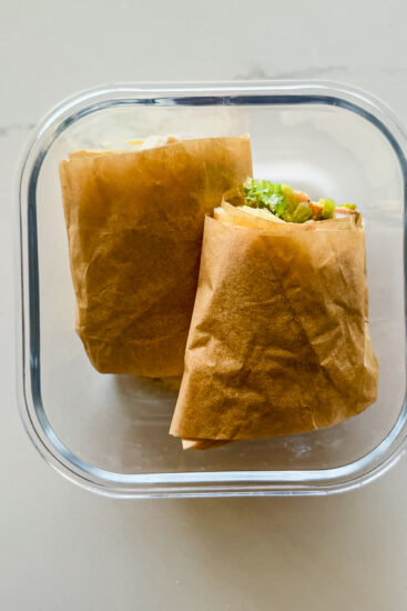 Healthy chicken caesar wraps in parchment paper in a meal prep container.