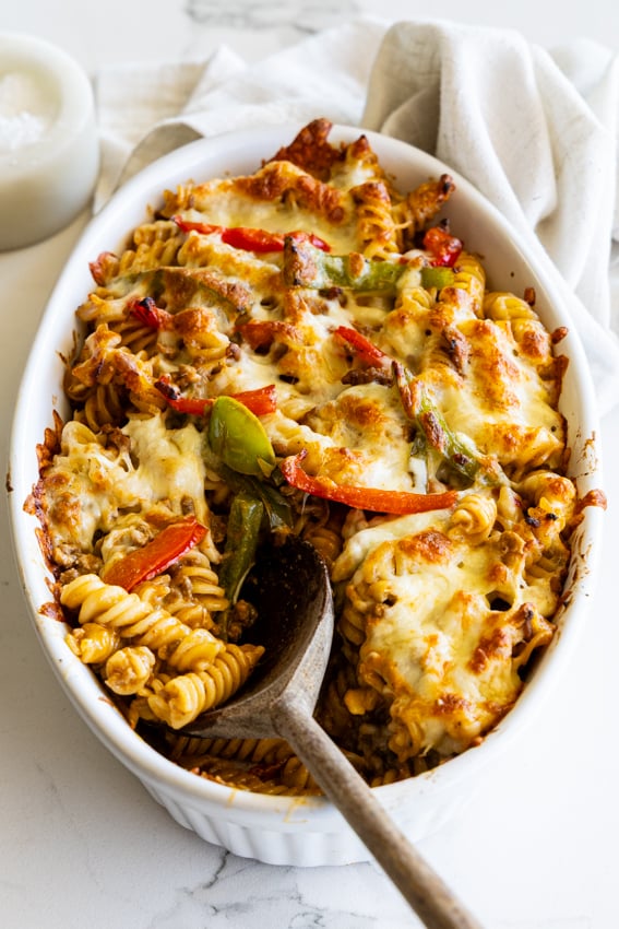 Taco Pasta Bake with peppers and cheese in an oval baking dish with a wooden spoon.