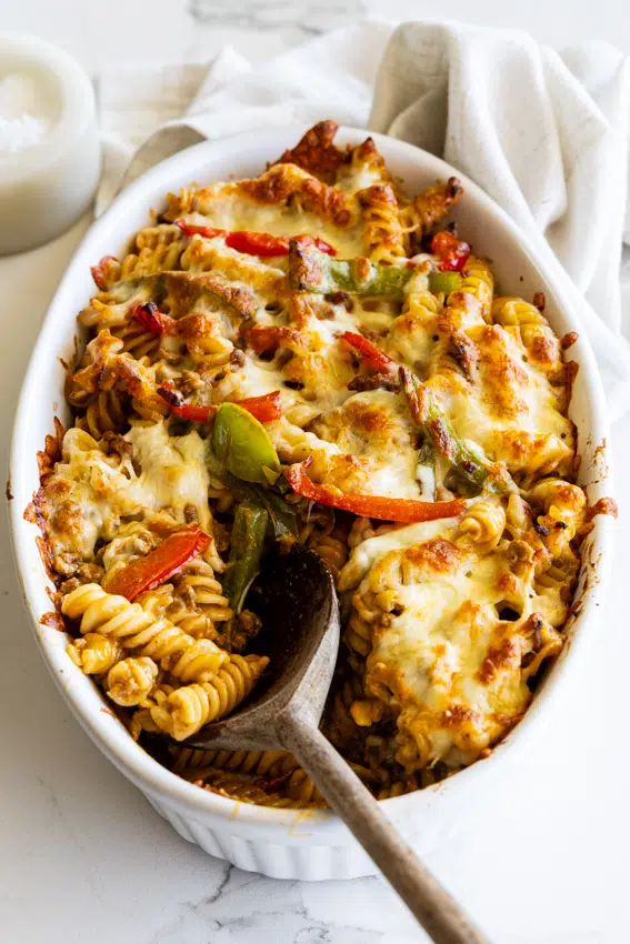 Taco Pasta Bake with peppers and cheese in an oval baking dish with a wooden spoon.