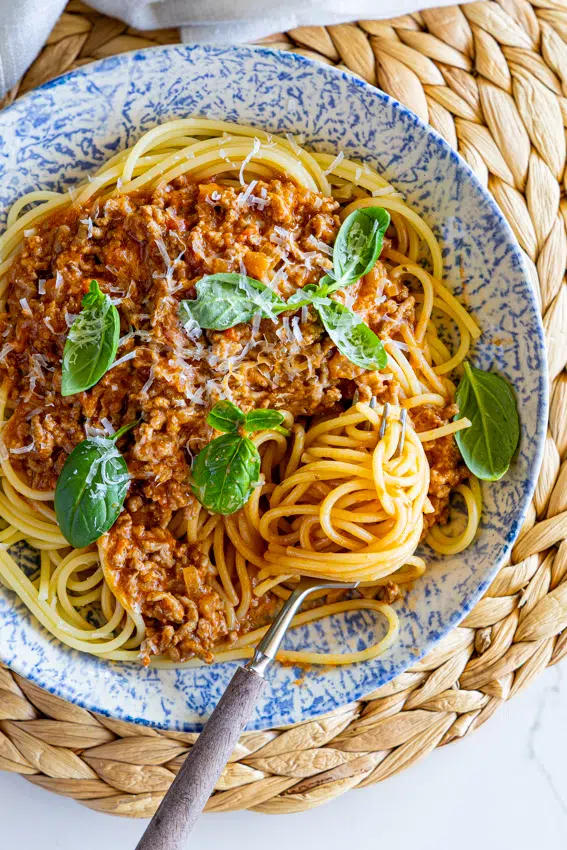 Creamy Tomato Beef Pasta in serving bowl with fresh basil leaves.