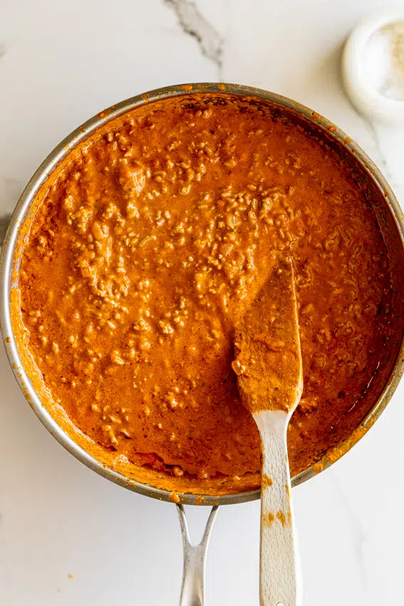 Creamy tomato beef pasta sauce in pan with wooden spatula.