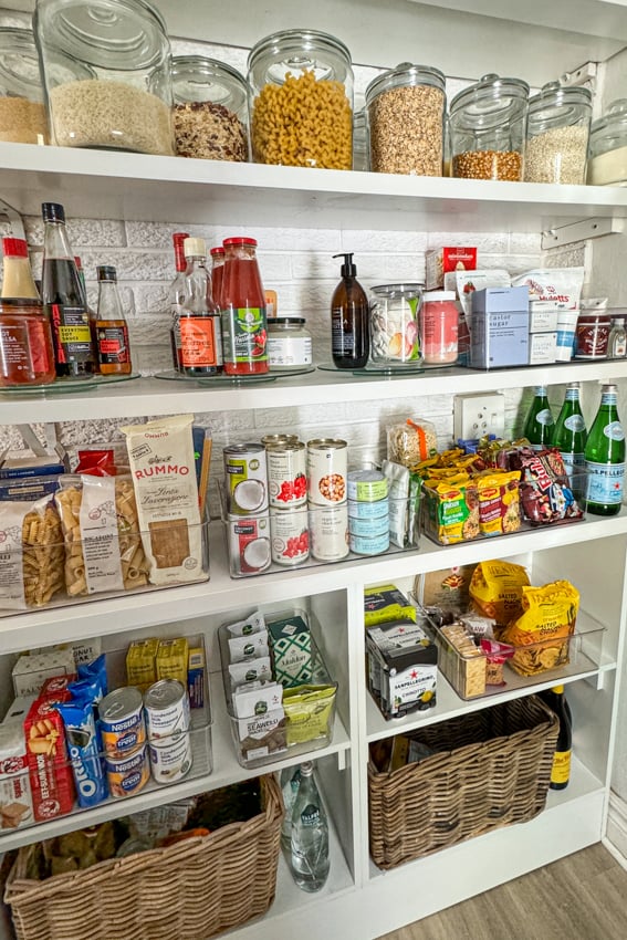 Stocked pantry with containers filled with canned foods, pasta, grains, snacks and condiments.