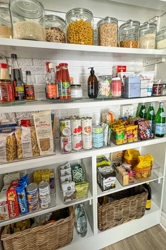 Stocked pantry with containers filled with canned foods, pasta, grains, snacks and condiments.