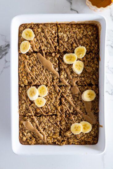 Baked oatmeal in baking dish topped with melted peanut butter and bananas.