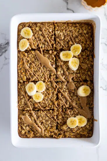 Baked oatmeal in baking dish topped with melted peanut butter and bananas.